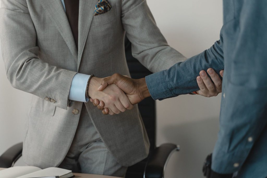 Imagem de um aperto de mão profissional entre dois homens de terno em uma reunião referente a uma operação de M&A.