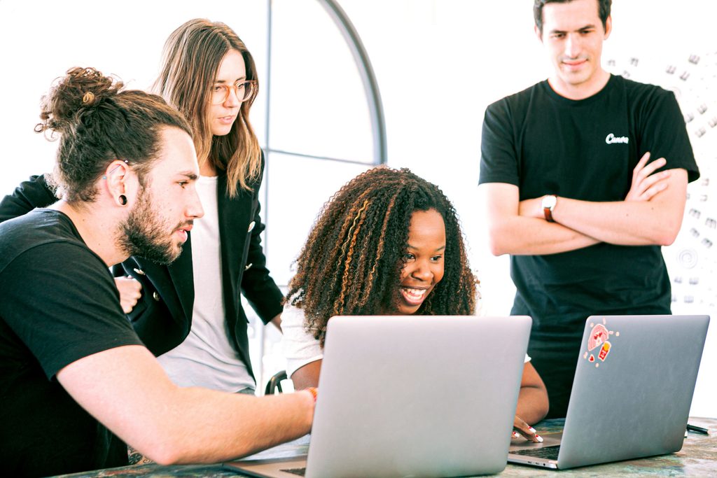Duas mulheres e dois homens olhando para duas telas de notebook, representando uma equipe em um treinamento de inglês para negócios.